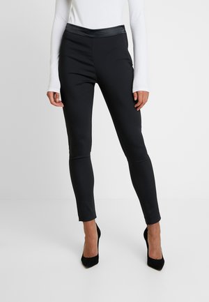 Leggings noirs en tissu lisse et extensible, avec un corps mat et une taille brillante, au design ajusté et à la coupe longueur cheville.