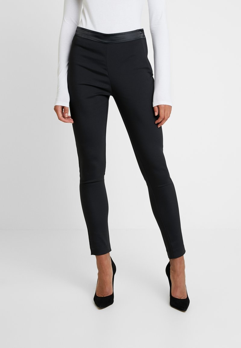 Schwarze Leggings aus einem glatten, dehnbaren Stoff, mit einem matten Körper und glänzendem Bündchen, eng anliegendem Design und knöchellanger Schnitt.