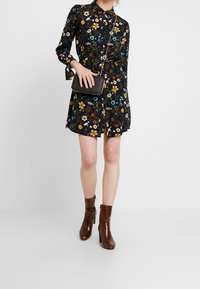 Blommönstrad klänning med marinblå bakgrund, långa ärmar, krage och indragen midja. Matchad med en svart axelremsväska och bruna klackstövlar.