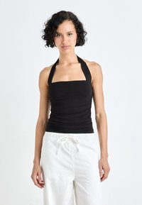 Black halter top with a square neckline and ruched texture, paired with loose white pants featuring an adjustable drawstring waistband.