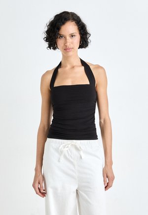 Haut halter noir avec un décolleté carrée et une texture froncée, associé à un pantalon blanc ample avec une ceinture ajustable à cordon.