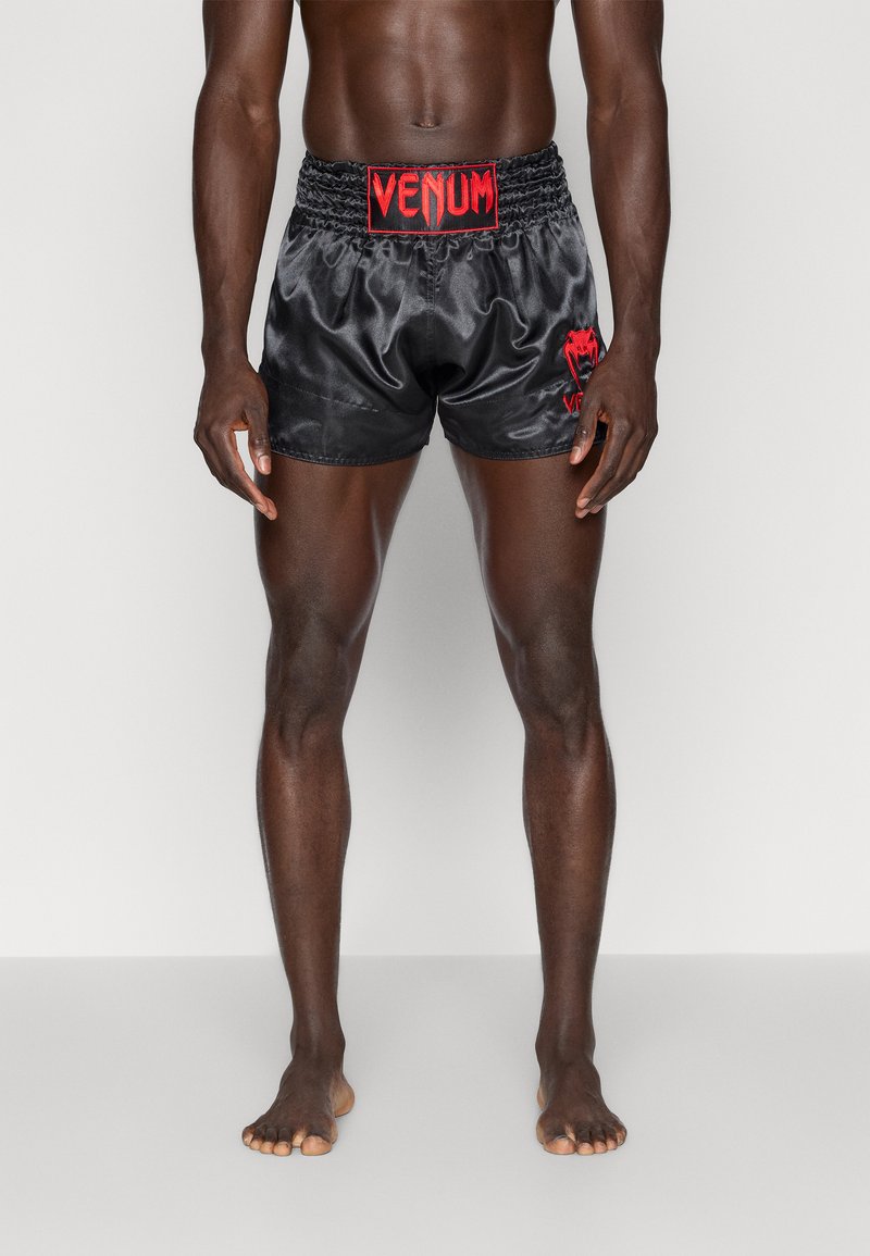 Calções de boxe em cetim preto com o logótipo vermelho "VENUM" na cintura e na lateral. Apresenta uma cintura elástica e uma textura suave. Sem bolsos.