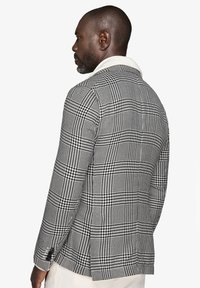 Blazer a quadri bianco e nero con colletto a revers, vestibilità strutturata e sottile motivo pied-de-poule, visto da dietro.