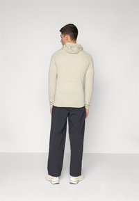 Vaaleanbeige pitkähihaisen hupparin, jossa on textured-kuvio, yhdistettynä tummiin, löysiin housuihin ja vaaleanvärisiin lenkkareihin.