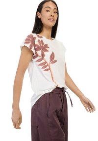 Kurzes, weißes T-Shirt mit floralem Design in Rosa und Orange, kombiniert mit dunkelvioletten Jogginghosen mit Kordelzug. Lässig, entspannte Passform.