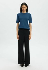 Sininen lyhythihainen neulepaita yhdistettynä mustiin löysiin housuihin ja teräväkärkisiin mustiin korkokenkiin. Sileä rakenne, hienovarainen muotoilu ja siistit linjat.