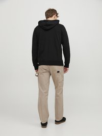 Zwarte hoodie met een trekkoord, gecombineerd met beige cargobroek met zijzakken en patches. Zwarte schoenen maken de outfit compleet.