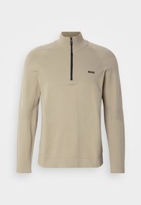 Beige långärmad tröja med svart halvdragkedja och "BOSS"-logotyp på vänstra bröstet, med hög krage och strukturerade tygdetaljer.