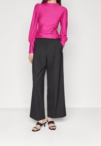 Fuchsia satintopp med långa ärmar och draperad detalj, kombinerat med högmidjade svarta vida byxor och svarta strappy klacksandaler.