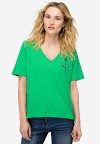 Grøn bomulds t-shirt med v-hals, korte ærmer og et sort ankerdesign på brystet. Stoffet ser blødt ud med en glat tekstur.