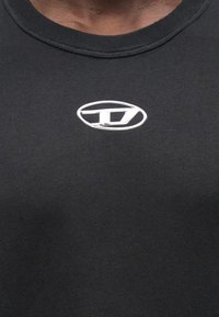 T-shirt preta de algodão com gola redonda e um logotipo metálico circular no centro, superfície texturizada, estilo justo.