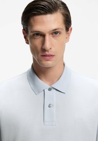 Jasnoszara koszulka polo wykonana z teksturowanej tkaniny, z kołnierzykiem, dwoma guzikami oraz subtelnym logo „BOSS” na piersi.