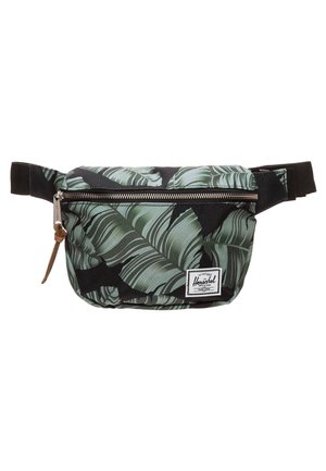 Sac banane avec motif feuilles tropicales noir et vert, poche zippée frontale, sangle noire réglable et étiquette de marque rectangulaire blanche.