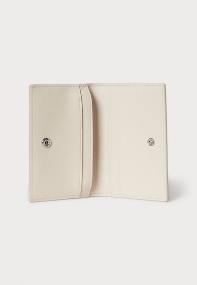 Kompaktni bež kožni novčanik otvoren ravno koji prikazuje utore za kartice i zatvarače na drukeru na bijeloj pozadini.