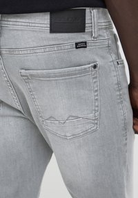 Lysegrå denim jeans båret af en person, der viser baglommen med et lille sort mærke og et syet design.