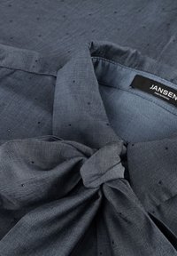 Donkerblauwe shirt met een geknoopte kraag, gemaakt van lichtgewicht stof met kleine, verhoogde stippen. Label leest "JANSEN AMSTERDAM."