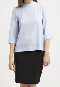Top azzurro chiaro con collo alto e maniche a tre quarti, abbinato a una gonna nera a coste lunghezza ginocchio. Tessuto dal tocco liscio.