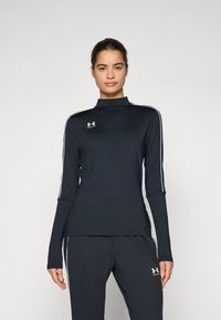 Black long-sleeve athletic top with a high collar, featuring white side stripes and a small logo on the left chest. Smooth, fitted fabric.