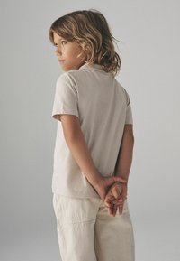 Ljusbeige t-shirt med korta ärmar, matchad med vitaktiga byxor. Enkelt mönster, mjuk textur, inga synliga mönster, enfärgad bakgrund.