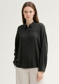 Black button-up shirt with a collar, made of a soft fabric. Features long sleeves and a relaxed fit, with a slightly textured surface.