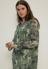 Vestido camisero de manga larga verde con estampado, en un material ligero y translúcido, con cuello tipo camisa y mangas ligeramente acampanadas.