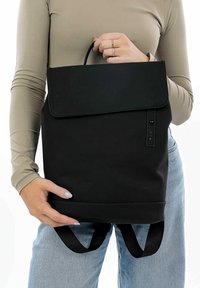 Czarna plecak wykonany z trwałego materiału, z klapą, uchwytem u góry i regulowanymi paskami na ramiona. Gładka tekstura, minimalistyczny design.