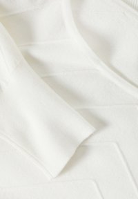 Gros plan sur la manche d'un pull en maille blanche et détail du tissu texturé avec des motifs géométriques de points.