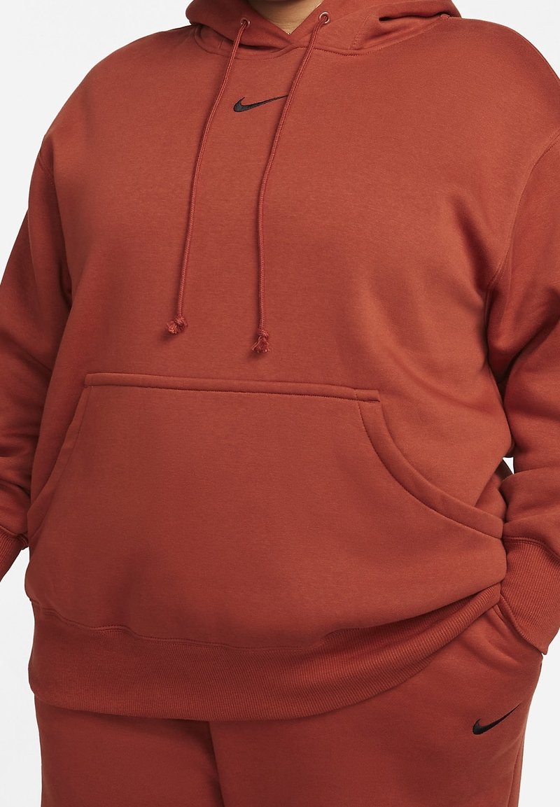 Sweat-shirt à capuche rouge avec une poche frontale, des détails de cordon de serrage, et un petit logo Nike noir sur la poitrine et en bas à gauche.