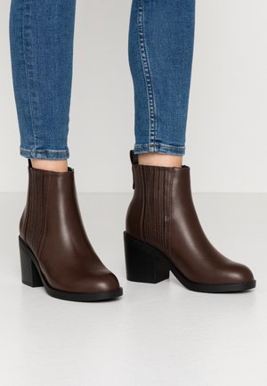 Braune Kunstleder-Ankle Boots mit einem dicken Absatz, die vertikale Rippakzente und eine Zuglasche hinten aufweisen.