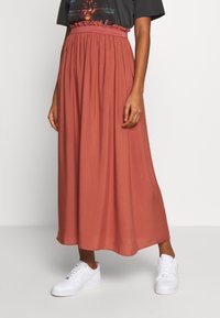 Maxi nederdel i rustfarve med elastisk talje og flæse detalje, lavet af letvægtsstof. Parret med hvide sneakers.