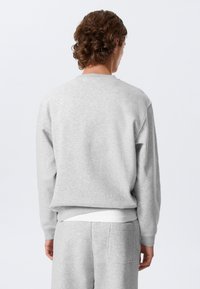 Siva majica dugih rukava opuštenog kroja, teksturirane tkanine, okruglog izreza i rebrastih manšeta. Uparena sa sivim hlačama koje imaju stražnji džep.