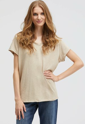 Beige Kurzarmoberteil mit Rundhalsausschnitt, weicher Textur und lockerer Passform. Kombiniert mit blauen Jeans; minimalistisches Design, ohne Muster oder Akzente.