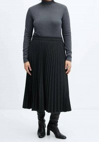 Falda midi negra plisada con cintura ajustada, combinada con una camiseta gris de manga larga. Modelo con botas negras de tacón hasta la rodilla.