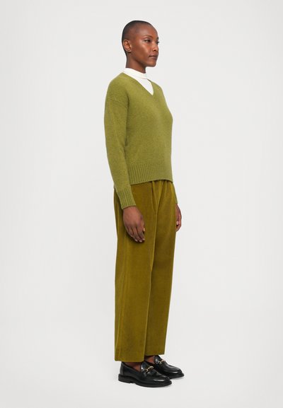 Green v-neck sweater made of soft material, paired with wide mustard corduroy pants. Black loafers with hardware detail complete the outfit.