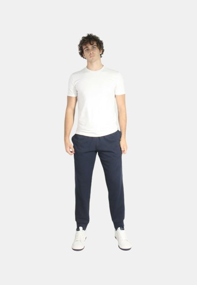 T-shirt aderente bianca e pantaloni felpati blu navy, abbinati a sneaker bianche. L'outfit presenta un design semplice e pulito senza modelli visibili.