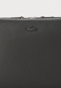 Borsa nera texturizzata con logo impresso in modo discreto, chiusura con zip e design elegante, realizzata in materiale resistente con una finitura liscia.