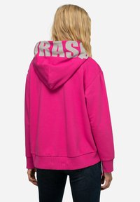 Hoodie rosa con scritte grigie sulla cappuccio. Presenta una vestibilità comoda, tasca a marsupio e polsini e orlo a costine. Tessuto morbido e testurizzato.