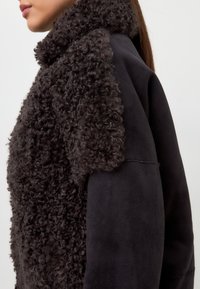 Chaqueta de piel de oveja negra con un cuello rizado texturizado y mangas suaves, que enfatiza los materiales contrastantes y la profundidad en el diseño.