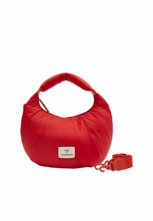 Sac à main rembourré en forme de croissant rouge, avec une poignée courte, une longue bandoulière détachable, et une étiquette blanche rectangulaire portant l'inscription « UNIO x THE VISIONNAIRES ».