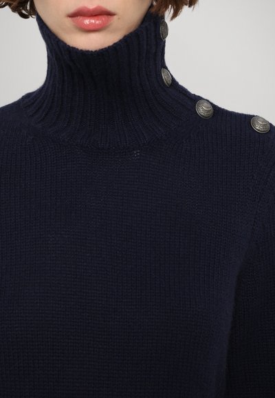 Pull col roulé bleu marine en tissu tricoté côtelé, avec trois boutons décoratifs en argent sur l'épaule.