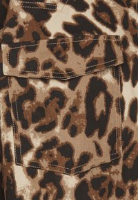 Leopard print fabric featuring shades of brown and black, with a prominent pocket outlined in brown stitching. Textured surface.