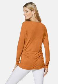 Langärmliges Hemd in verbranntem Orange, mit lässiger Passform und gerafftem Detail auf der Rückseite, aus weichem, dehnbarem Stoff gefertigt.