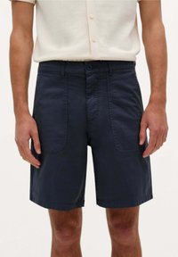Shorts en coton bleu marine avec fermeture à boutons, deux poches avant plaquées et un ourlet droit. Texture lisse avec une coupe décontractée.