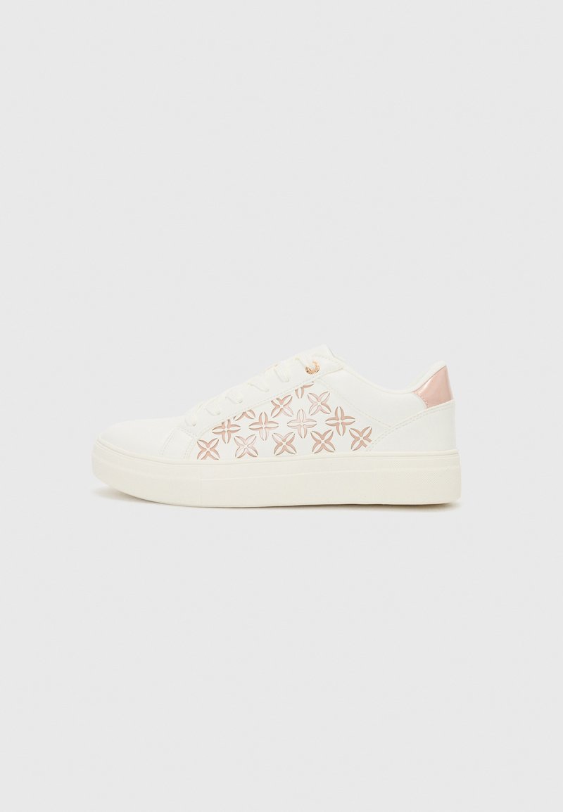 Sneaker bianca con motivo floreale rosa sul lato, parte superiore in tela texturizzata, suola piatta in gomma e accentuazione rosa sul tallone.
