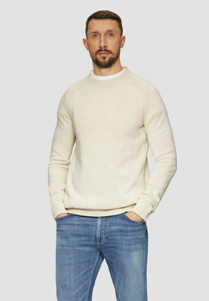 Crèmekleurige gebreide trui met geribde manchetten en zoom, voorzien van een textuurpatroon. Draagt met lichtblauwe jeans.