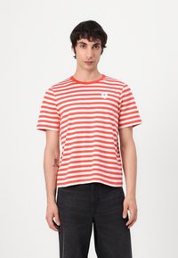 Tricou scurt cu mâneci, cu dungi roșii și albe, gât rotund și un detaliu grafic mic alb pe piept. Fabricat din material de bumbac.