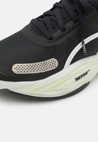 Schwarze Sneakers aus Mesh-Gewebe, mit strukturierten Akzenten, einem PWR-Band-Detail und einer weißen Zwischensohle mit einem gerippten, hellgrünen Abschnitt.