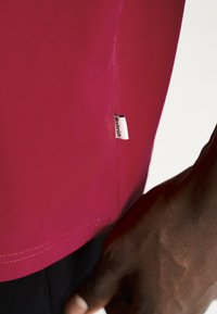 Tætsiddende kortærmet skjorte i livlig pink stof, med en søm der har et lille mærke og synlige syninger ved kanten.