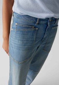 Lichtblauwe denim jeans hebben een relaxte pasvorm, meerdere zakken en subtiele stiksels. De stof heeft een licht versleten textuur en een gladde afwerking.