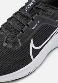 Svarte mesh løpesko med et slankt design, med en hvit swoosh aksent, teksturert overdel og synlig dempingsteknologi.